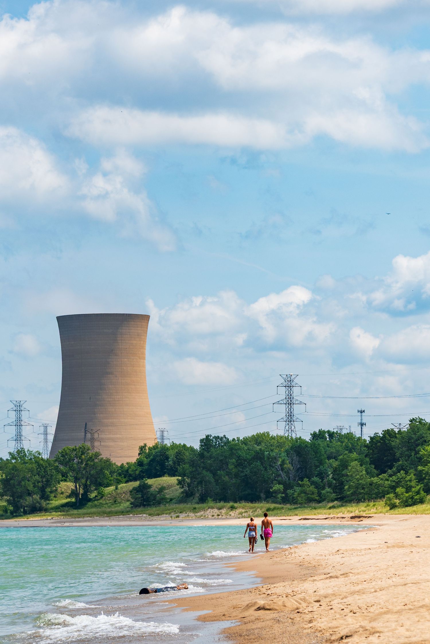 Nuclear cooling towers rise behind sandy beach on lake shore.