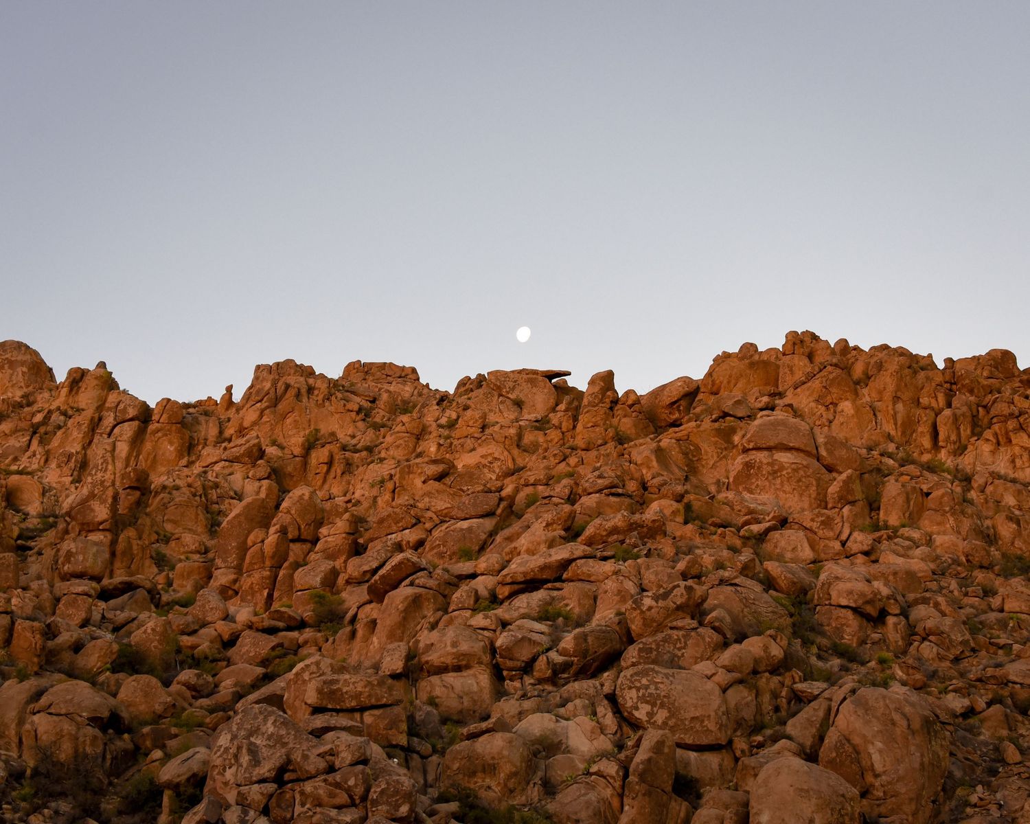 Rocky desert landscape with large boulders against a warm sunset sky.