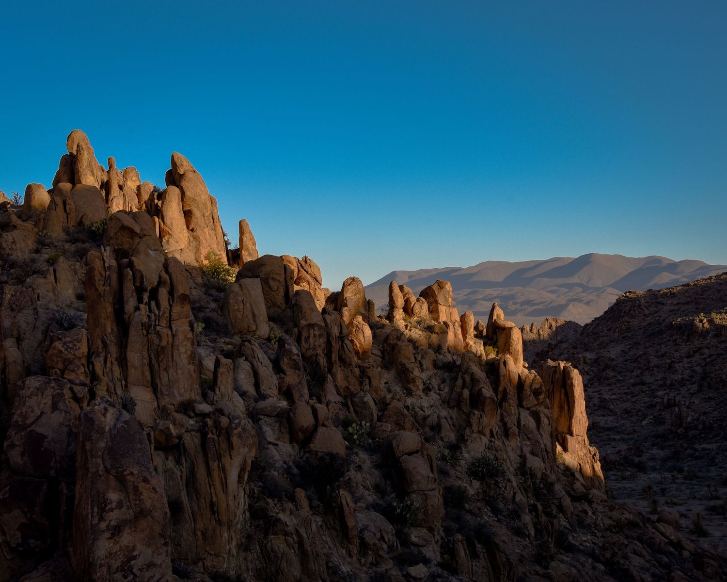 Rugged rock formations stand against a clear blue sky in a desert landscape.