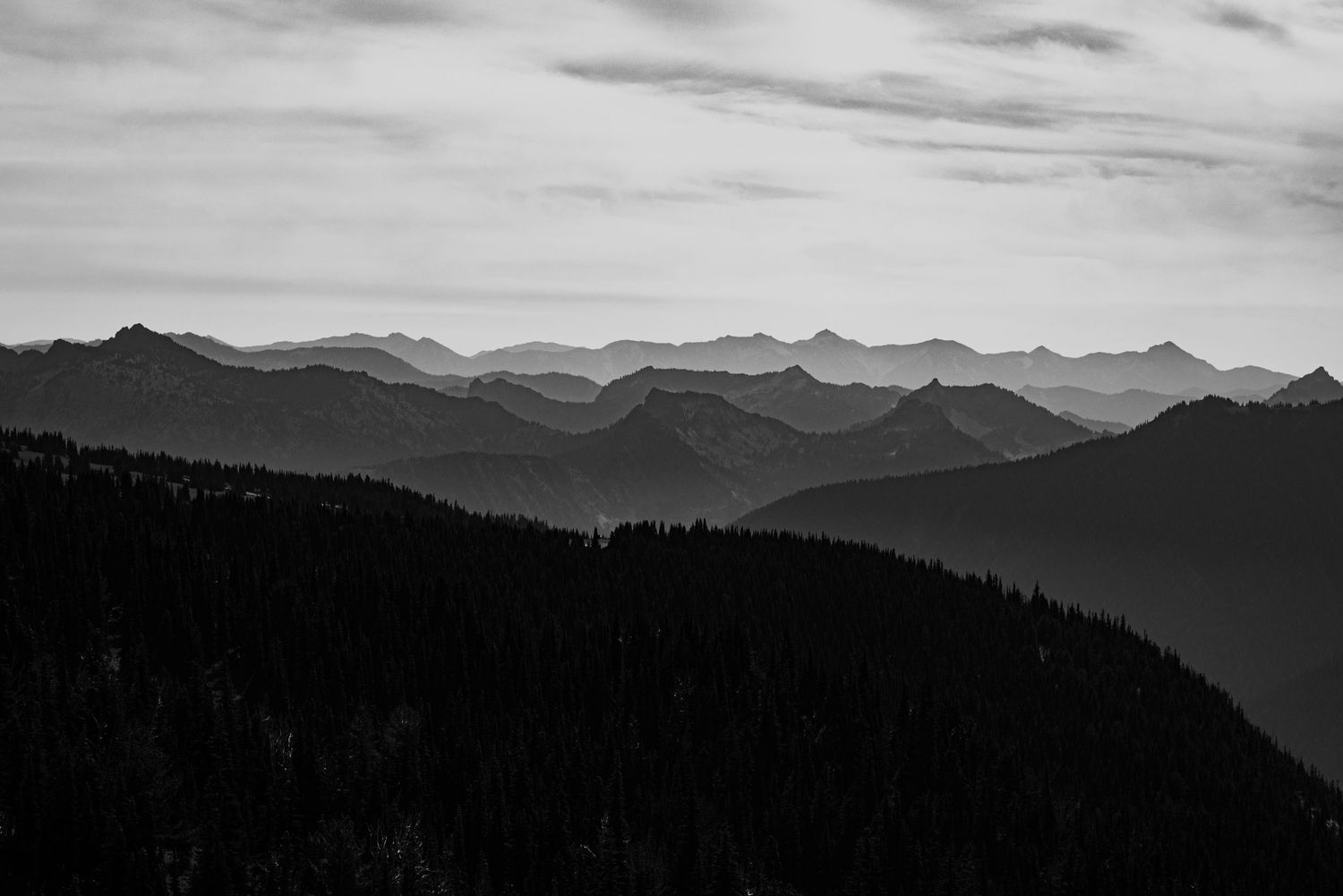 Silhouetted mountain ranges fade into misty distance in black and white landscape.