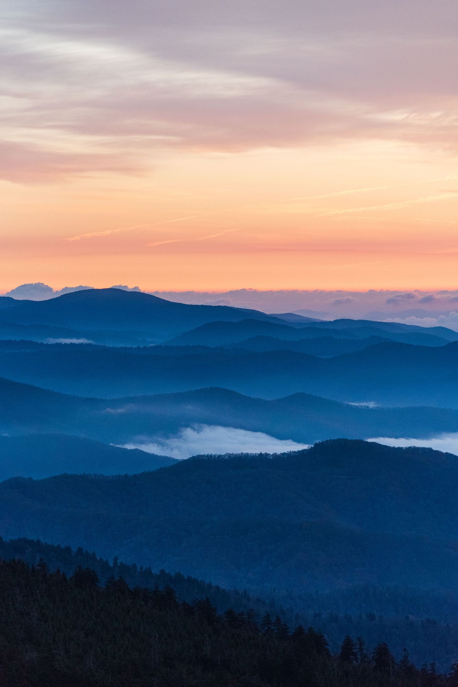 Misty mountain ranges at sunset with layered blue ridges stretching to the horizon.