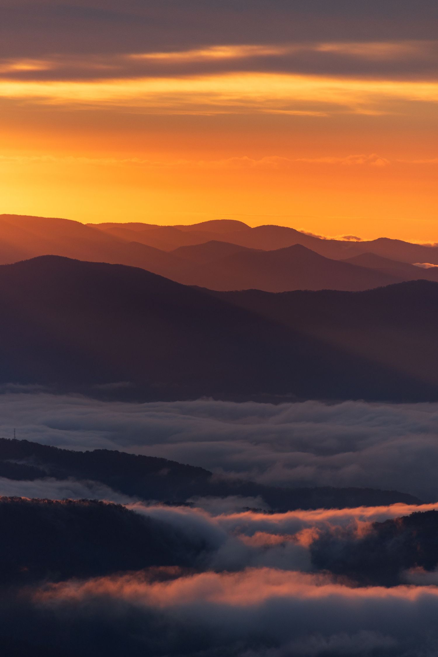 Stunning mountain sunset with fog rolling through valleys in orange and purple hues.