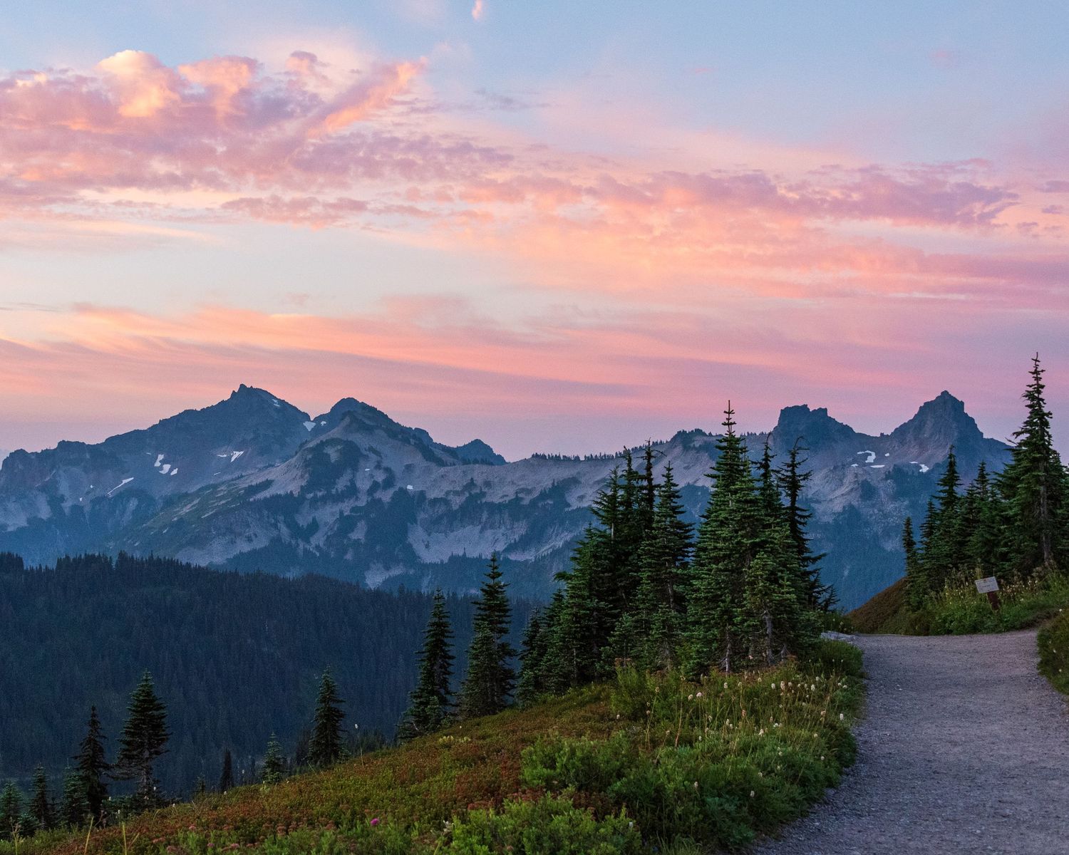 Mountain landscape with pink sunset clouds and snow-capped peaks along a winding trail.