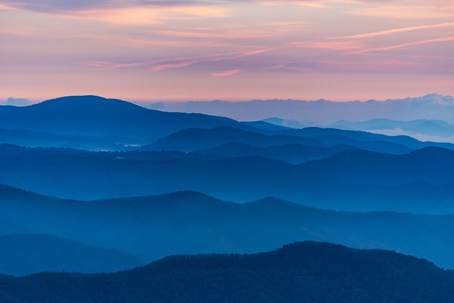 Layered mountain ridges fade into blue hues at sunset creating a peaceful landscape vista.