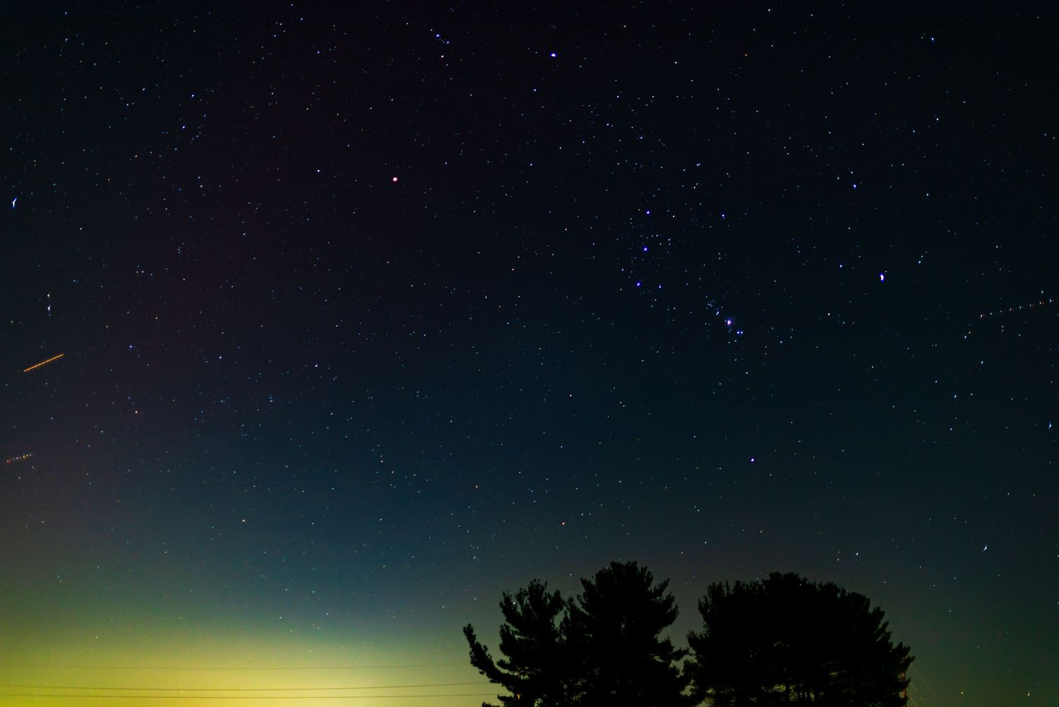 Green aurora borealis glows on the horizon beneath a starry night sky.