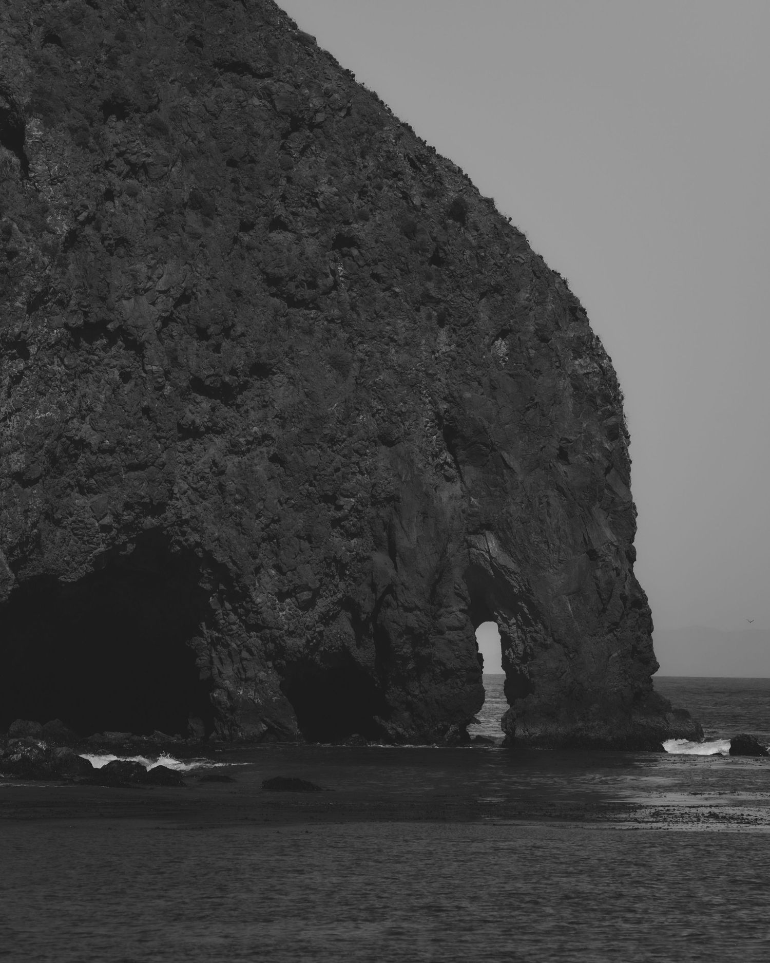 Dramatic black and white coastal rock formation with natural arches jutting into the ocean.