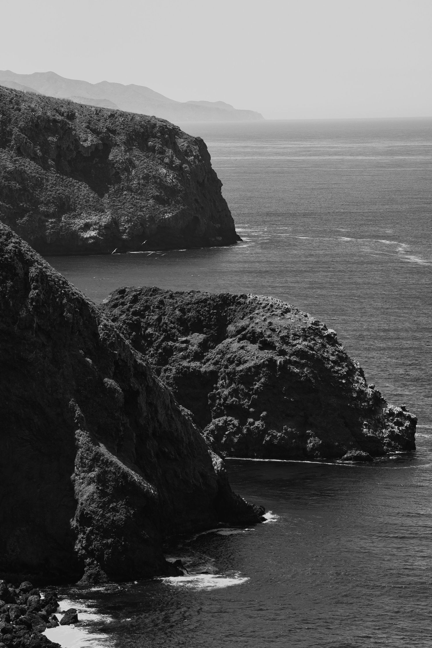 Rugged coastal cliffs and rocky headlands along a dramatic black and white seascape.