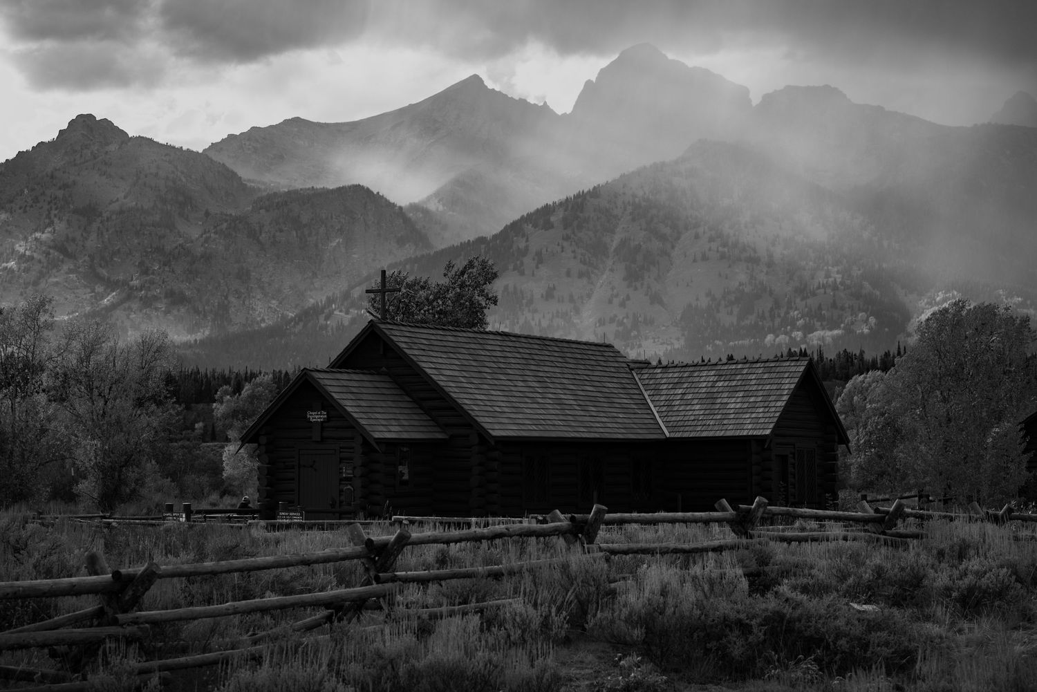 Black and white landscape of mountain barn silhouettes against misty peaks.