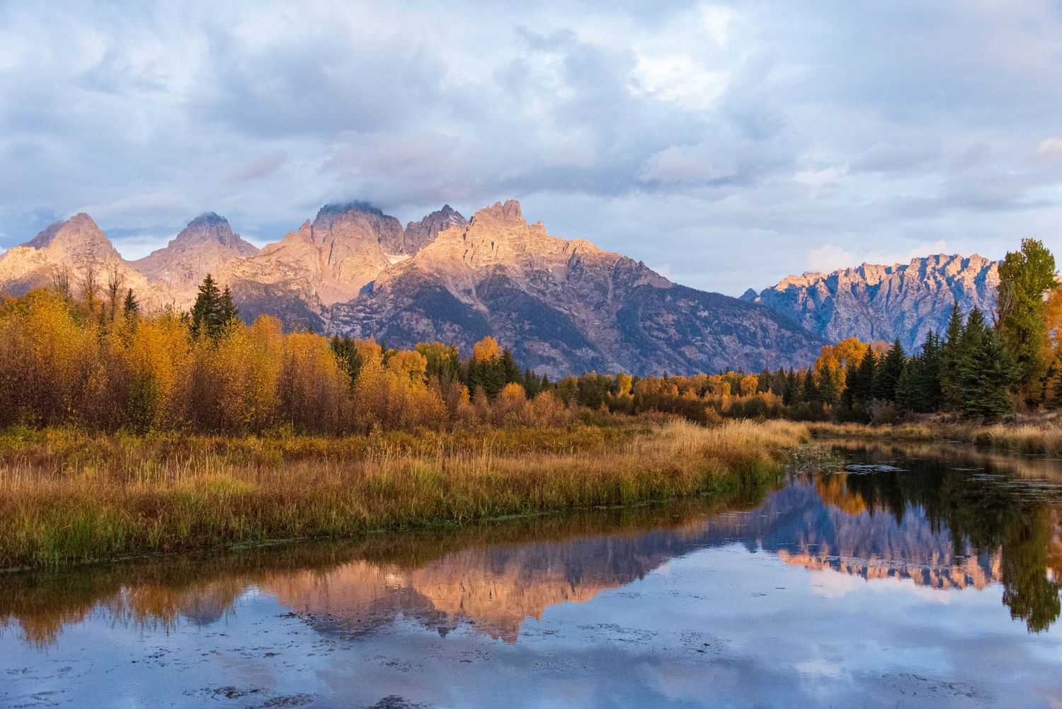 Snow-capped mountain peaks reflect in still waters during golden autumn light.