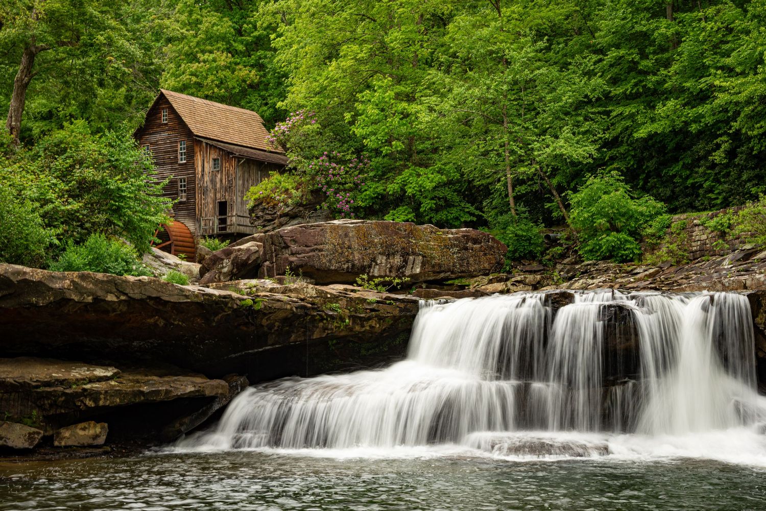 Scenic waterfall cascading over rocks with an old mill building visible through lush greenery.