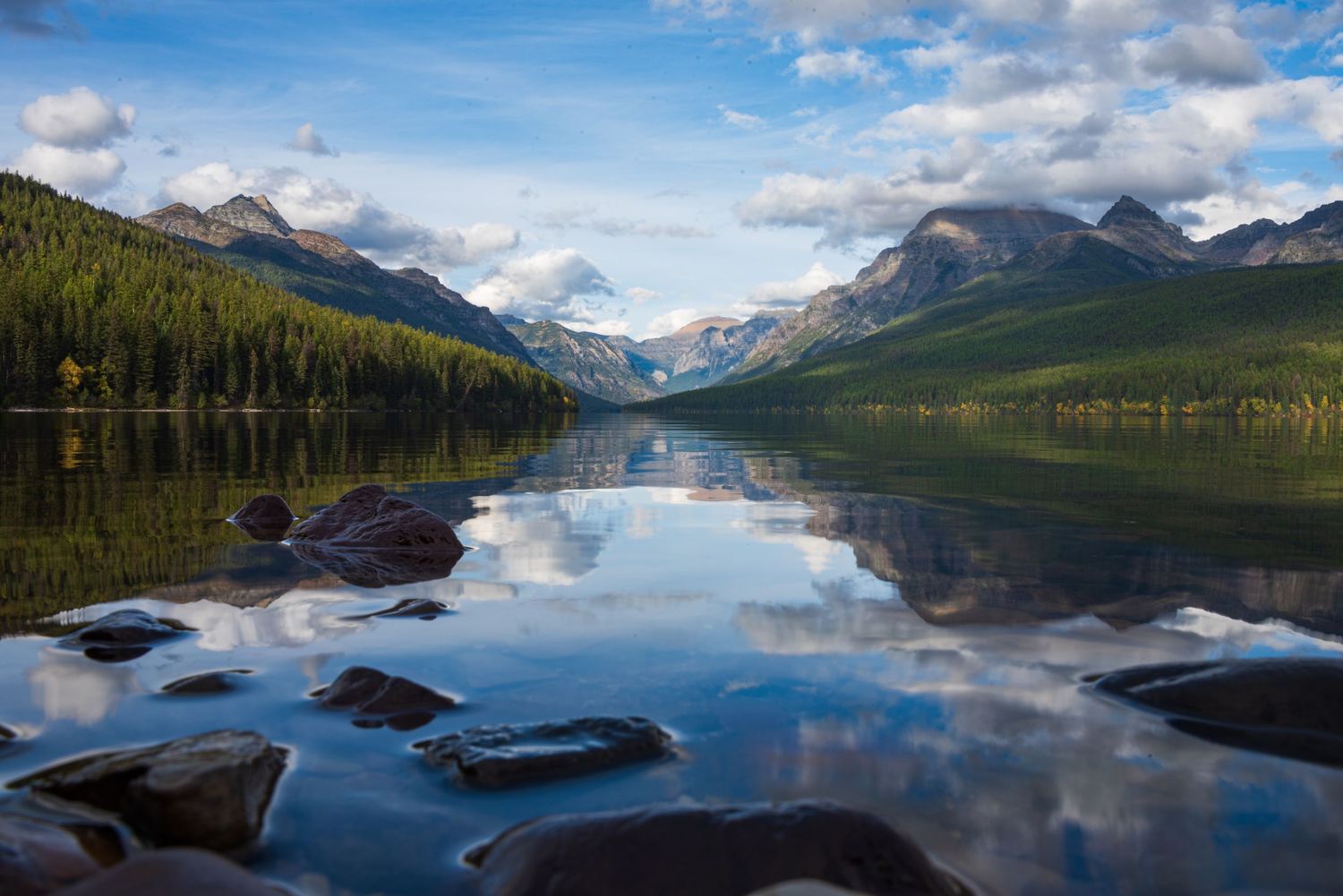 Serene mountain lake reflecting snow-capped peaks and clouds in mirror-like surface.