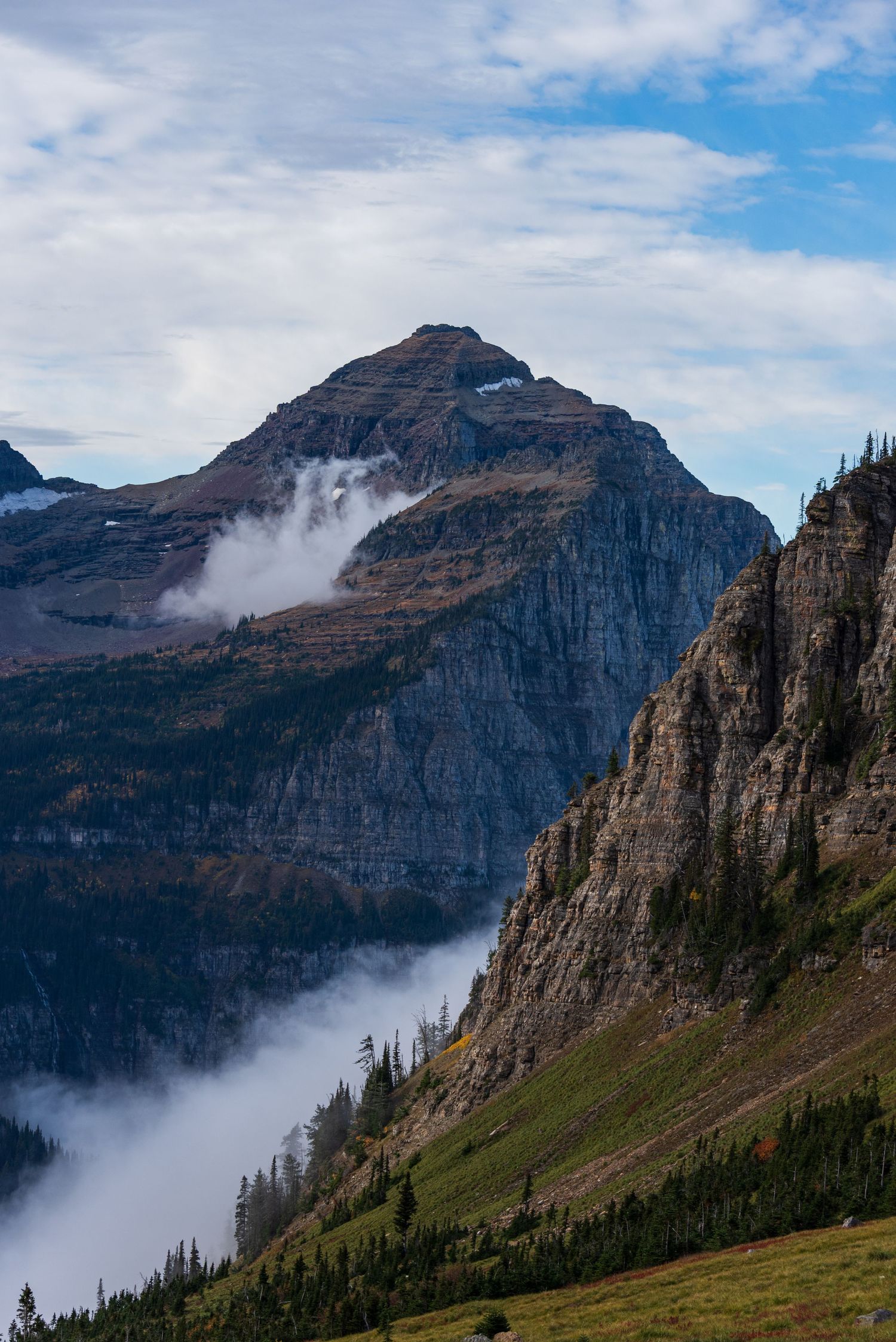 Dramatic mountain cliffs emerge from low-lying clouds in a rugged alpine landscape.