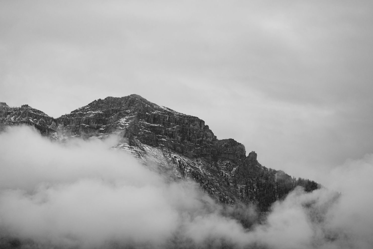 Misty clouds swirl around a dark mountain peak in black and white.