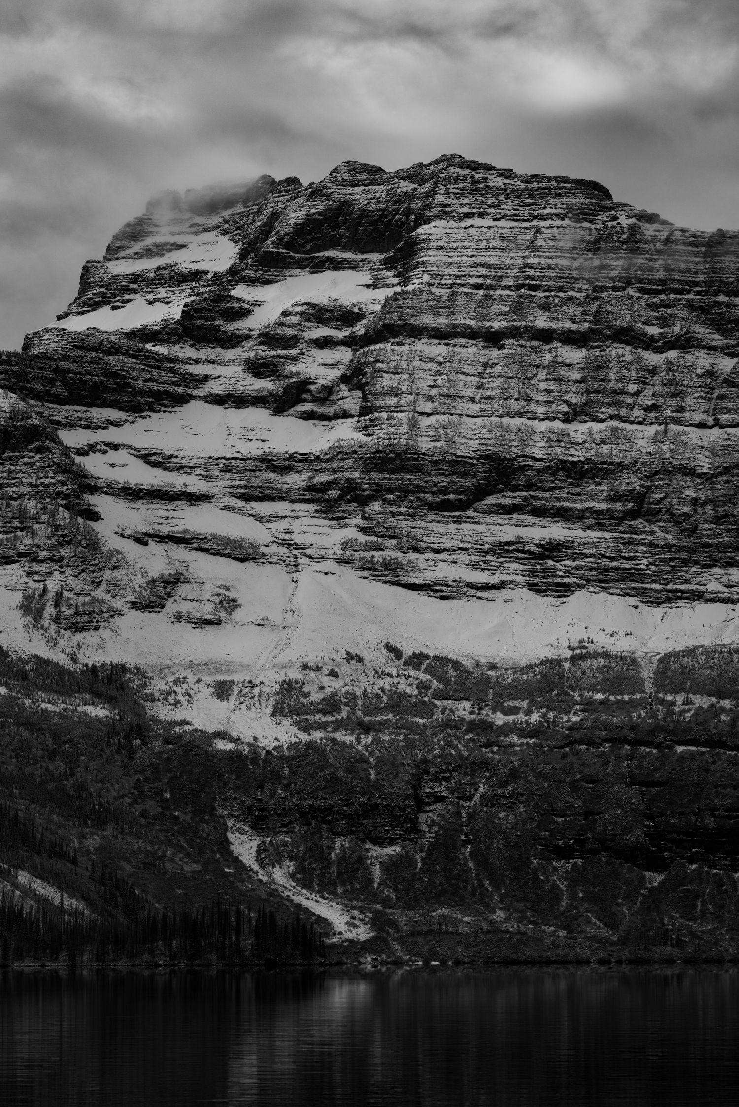 Dramatic black and white mountain cliffs reflected in still lake waters below.