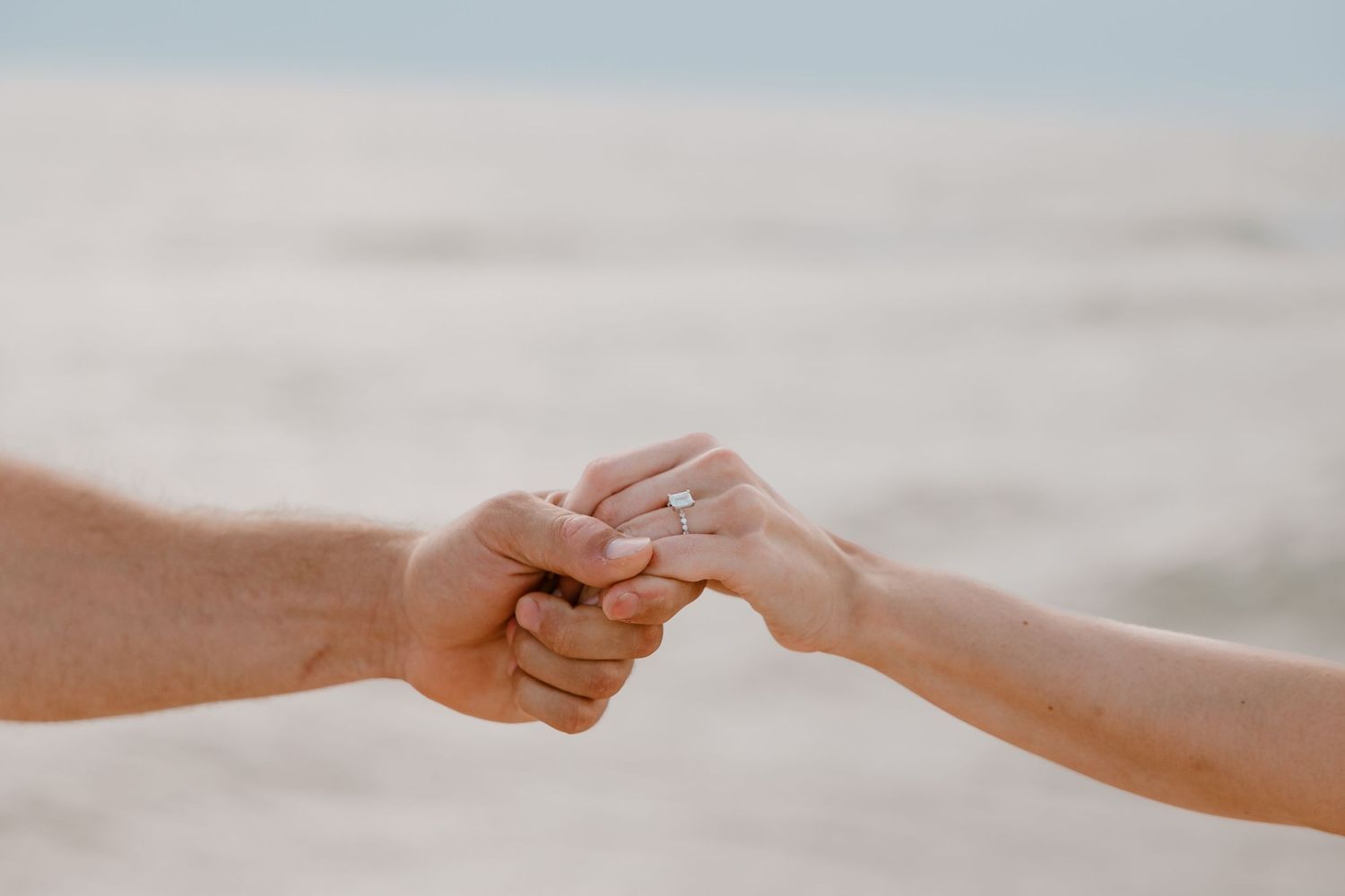 Two hands gently touch and hold each other against a soft blurred background during golden hour.