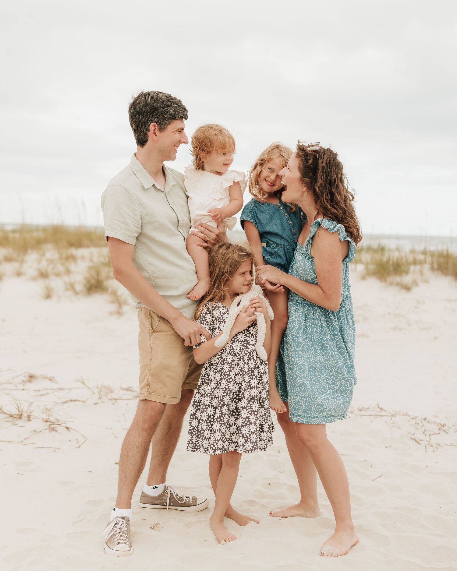Family wearing coordinated casual outfits pose together on a sandy beach during sunset.