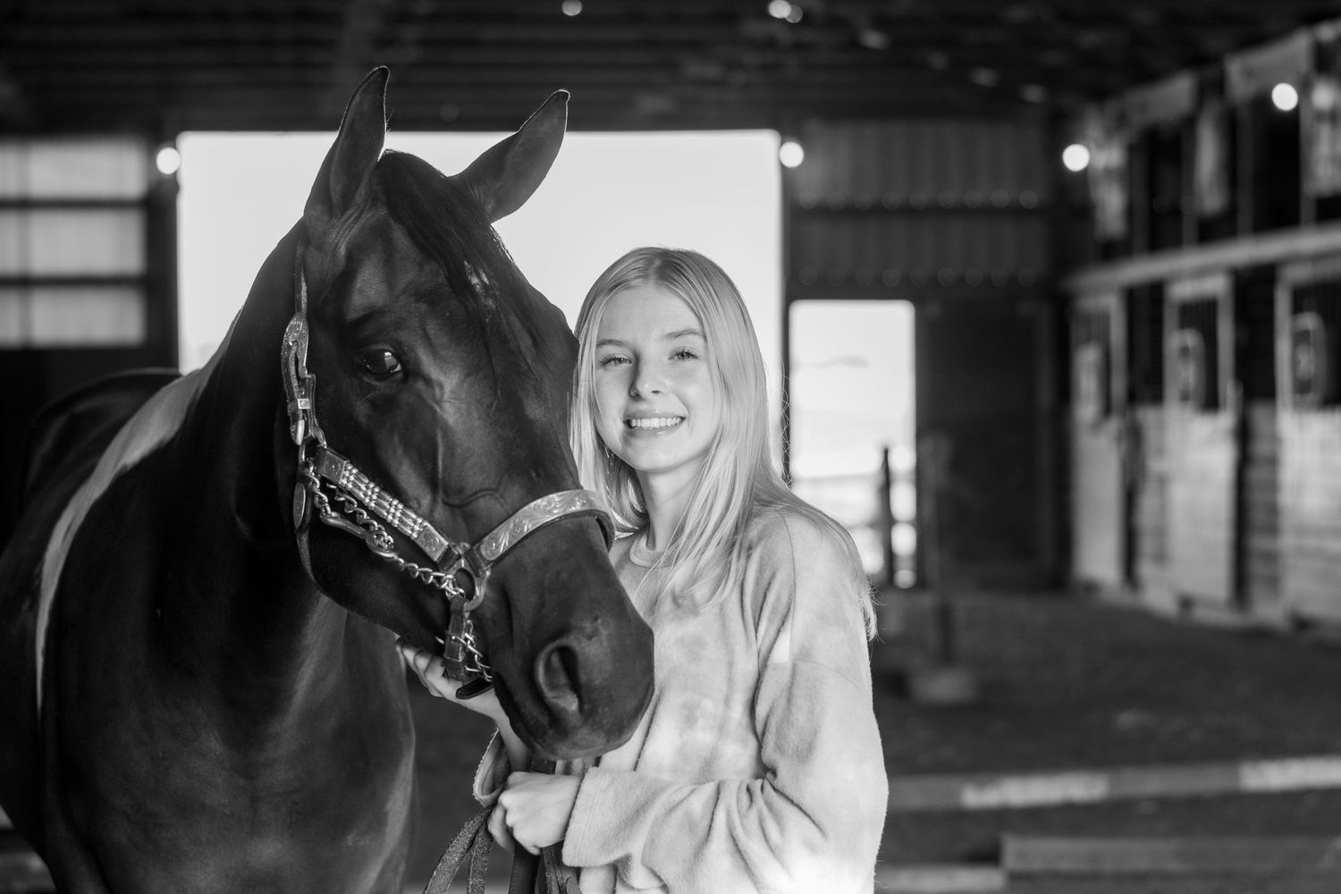 Black and white portrait of a senior girl smiling with her horse in the stables.