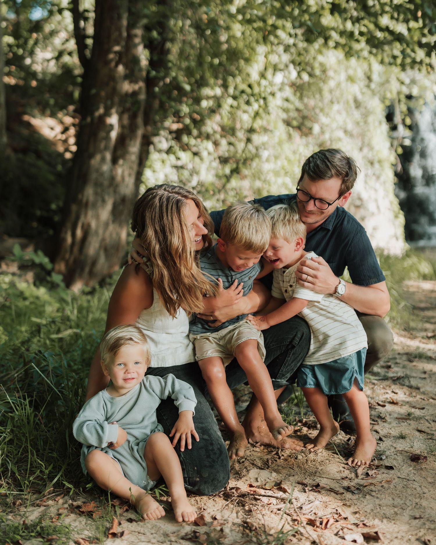 Family of four spending quality time together outdoors in a wooded setting during a casual photo session.