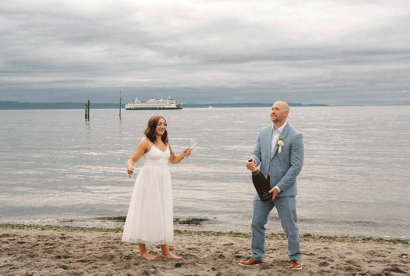 A couple in formal wear dances joyfully on a cloudy beach during a romantic moment by the ocean.