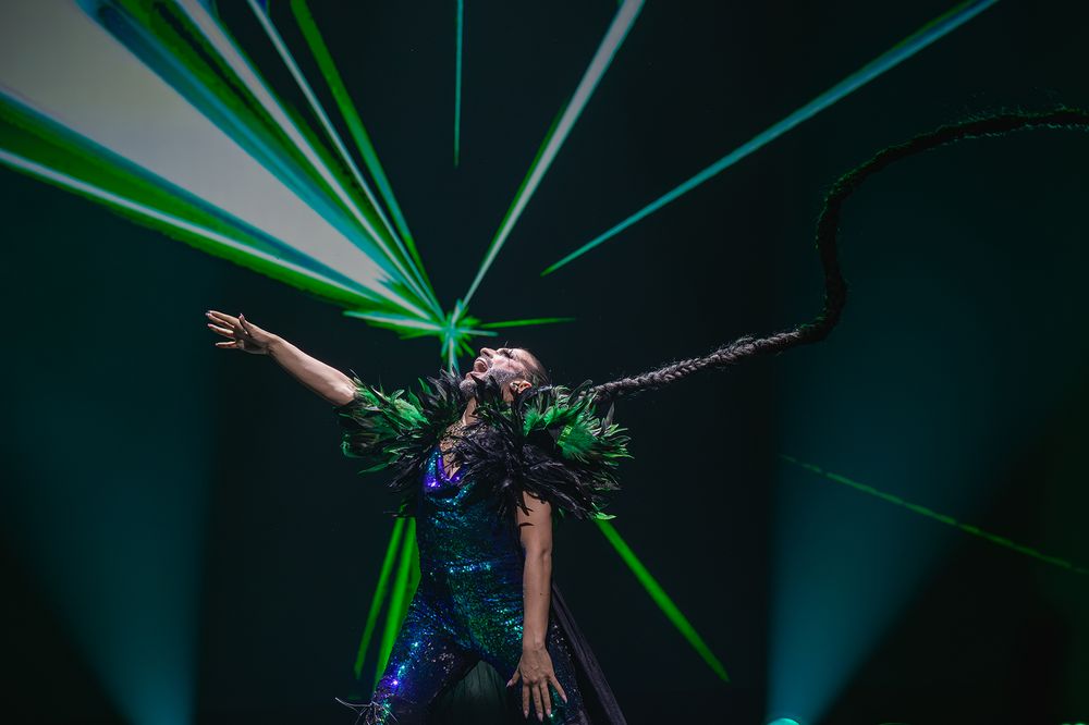 Drag performer with green laser lights creating dramatic aerial dance movements.