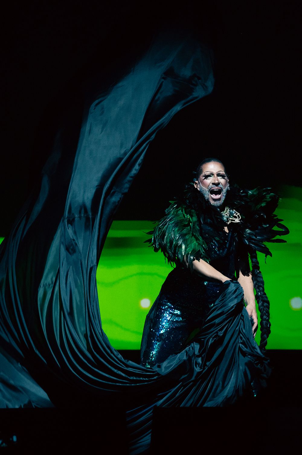 Theatrical performer in flowing black costume against dramatic green lighting.