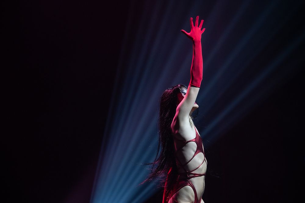 Dramatic silhouette of performer reaching upward with red lighting effects.