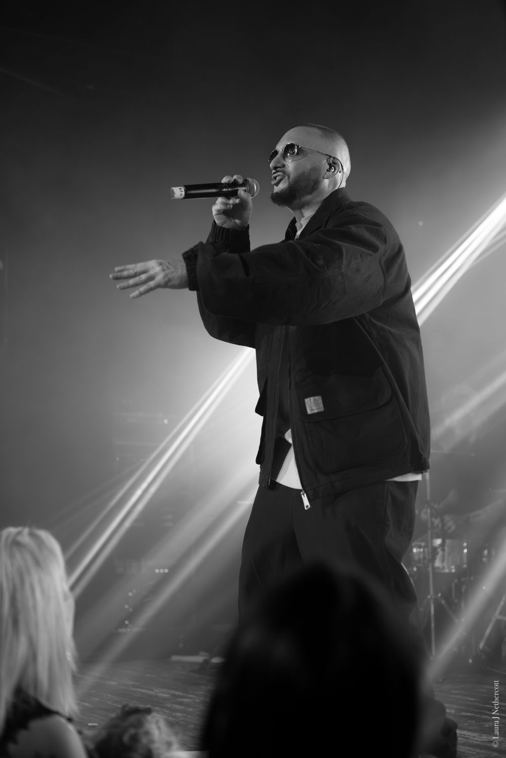 Performer on stage illuminated by dramatic lighting beams during live concert performance.