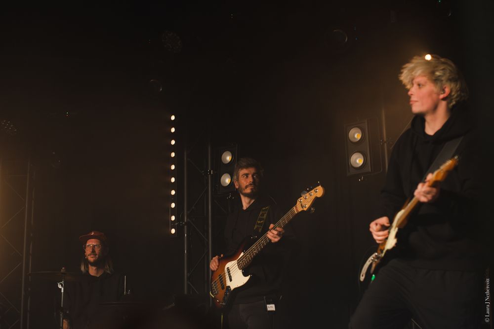 Musicians playing guitars on dimly lit stage during live performance.