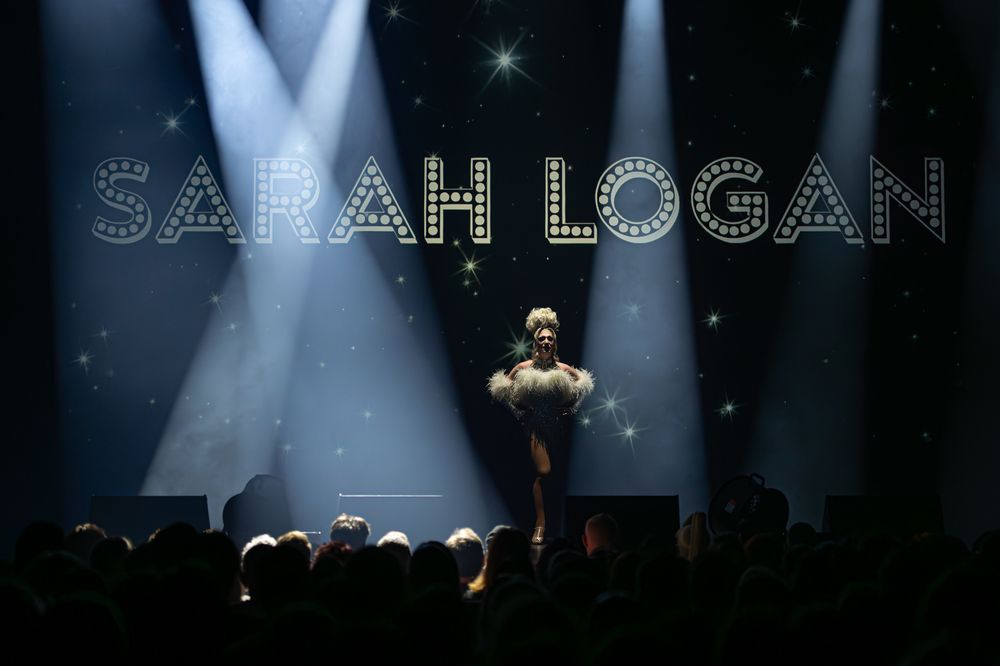 Stage performer under spotlights with illuminated text display above.