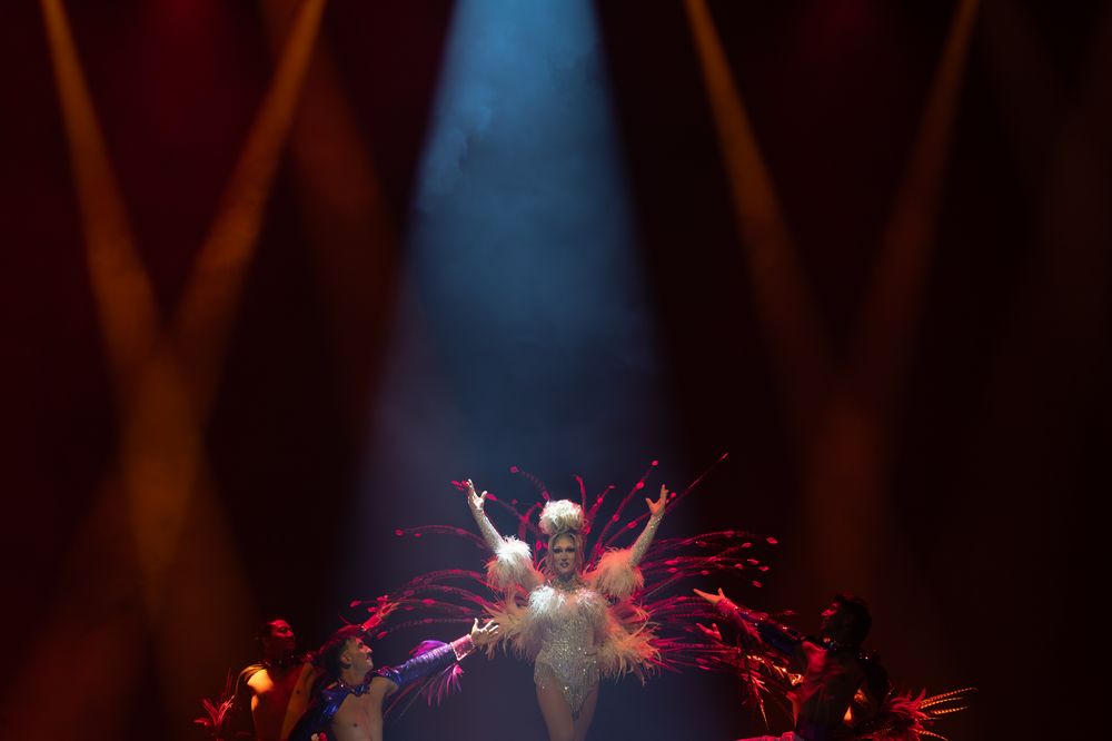 Performer in sparkly costume illuminated by dramatic red stage lighting and spotlights.