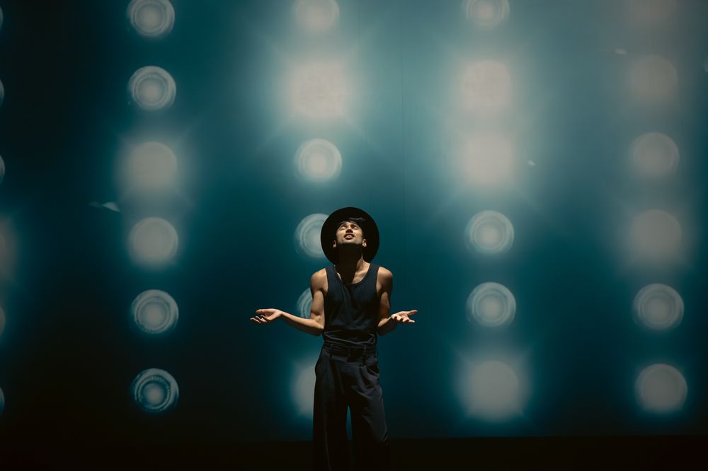 Performer in black outfit against blue bokeh lights creates dramatic silhouette on stage.