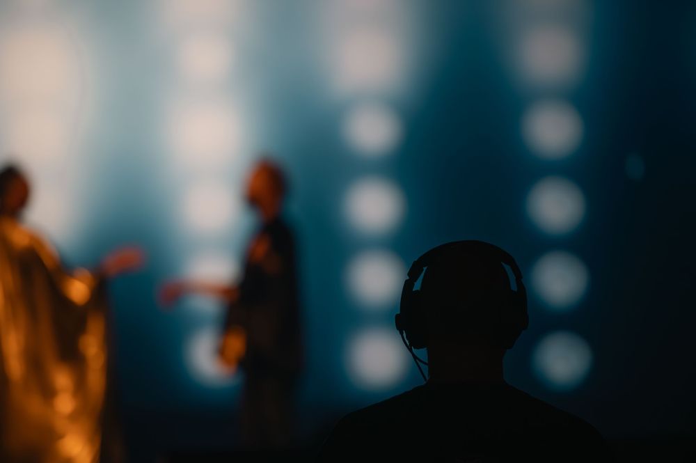 Concert crowd silhouettes against blurred blue and orange lighting effects.