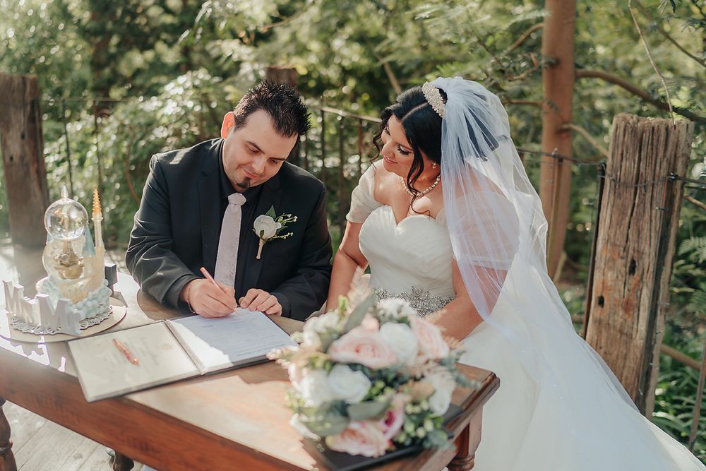 Marriage document signing ceremony taking place outdoors under wooden beams surrounded by forest greenery.