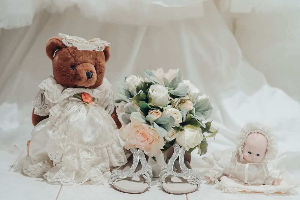 A collage of baby christening items including white gowns, soft teddy bears, silver shoes and delicate white flowers.