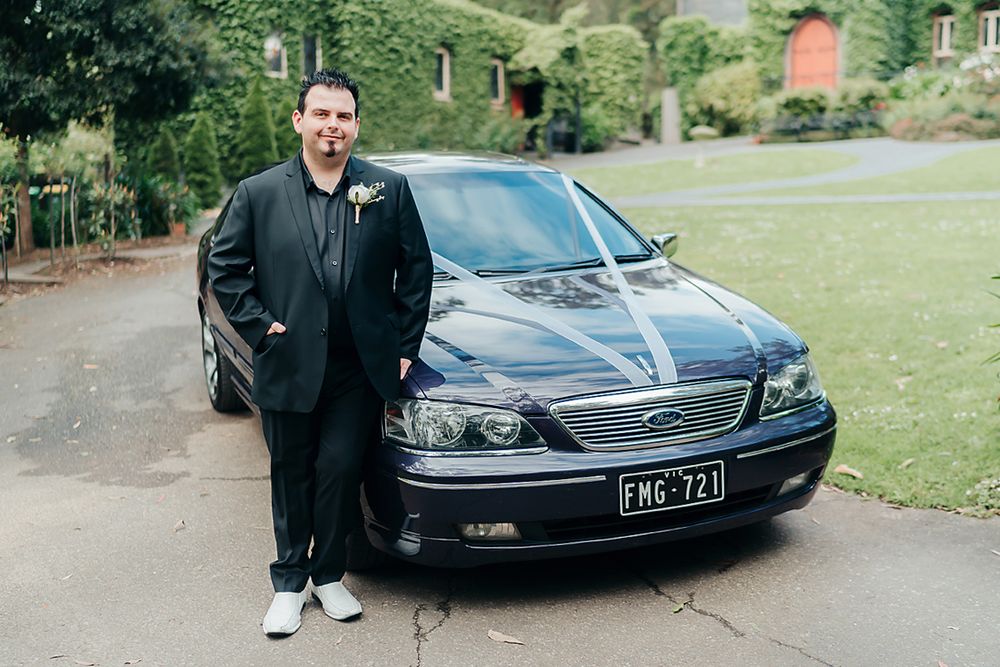 A glossy black Ford sedan parked on a gravel driveway with greenery in the background.