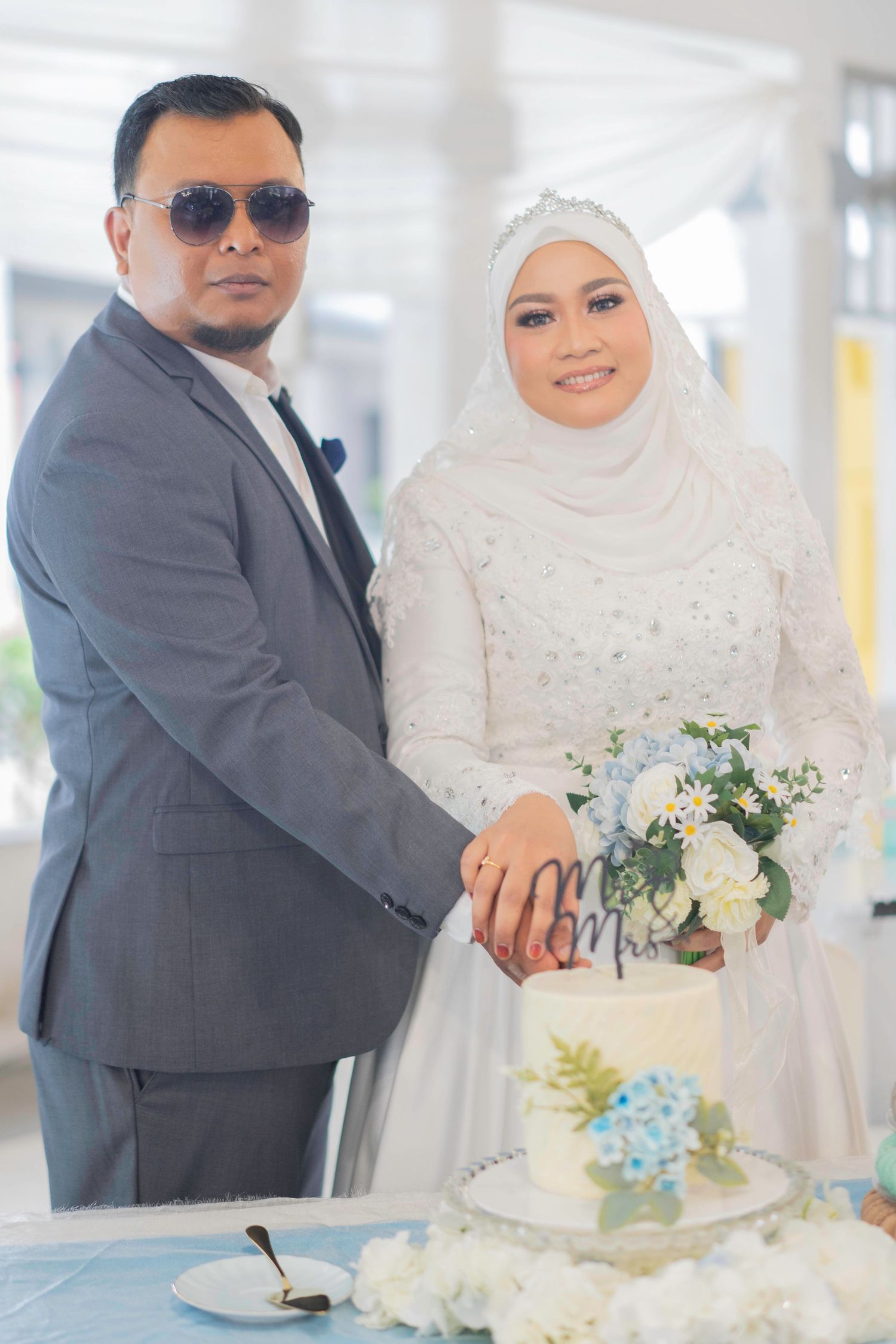 Beautiful wedding couple in formal attire cutting their white and blue wedding cake together at reception.
