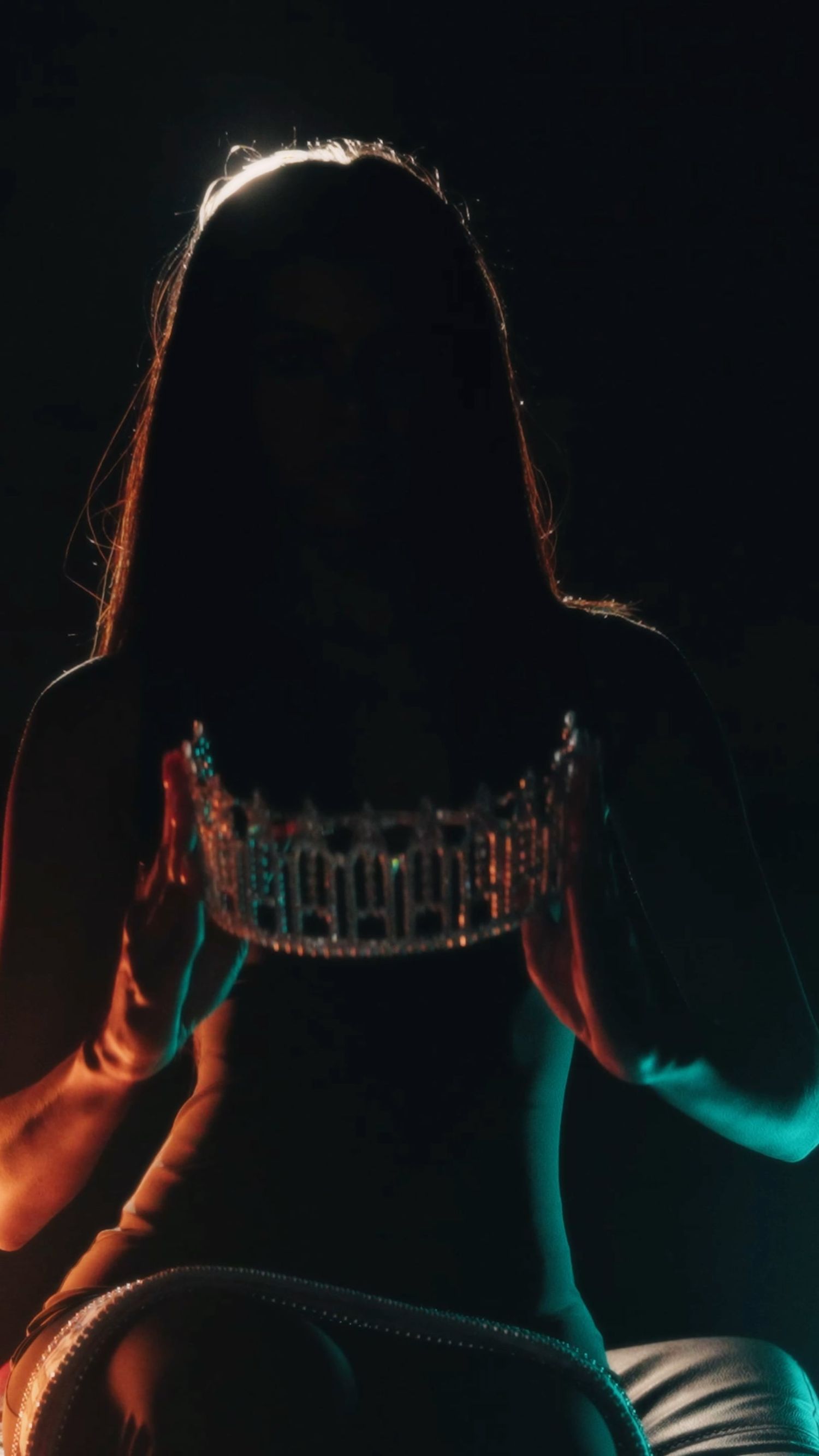 A backlit silhouette of a person wearing a sparkly top with colorful red and blue lighting effects in a dark setting.