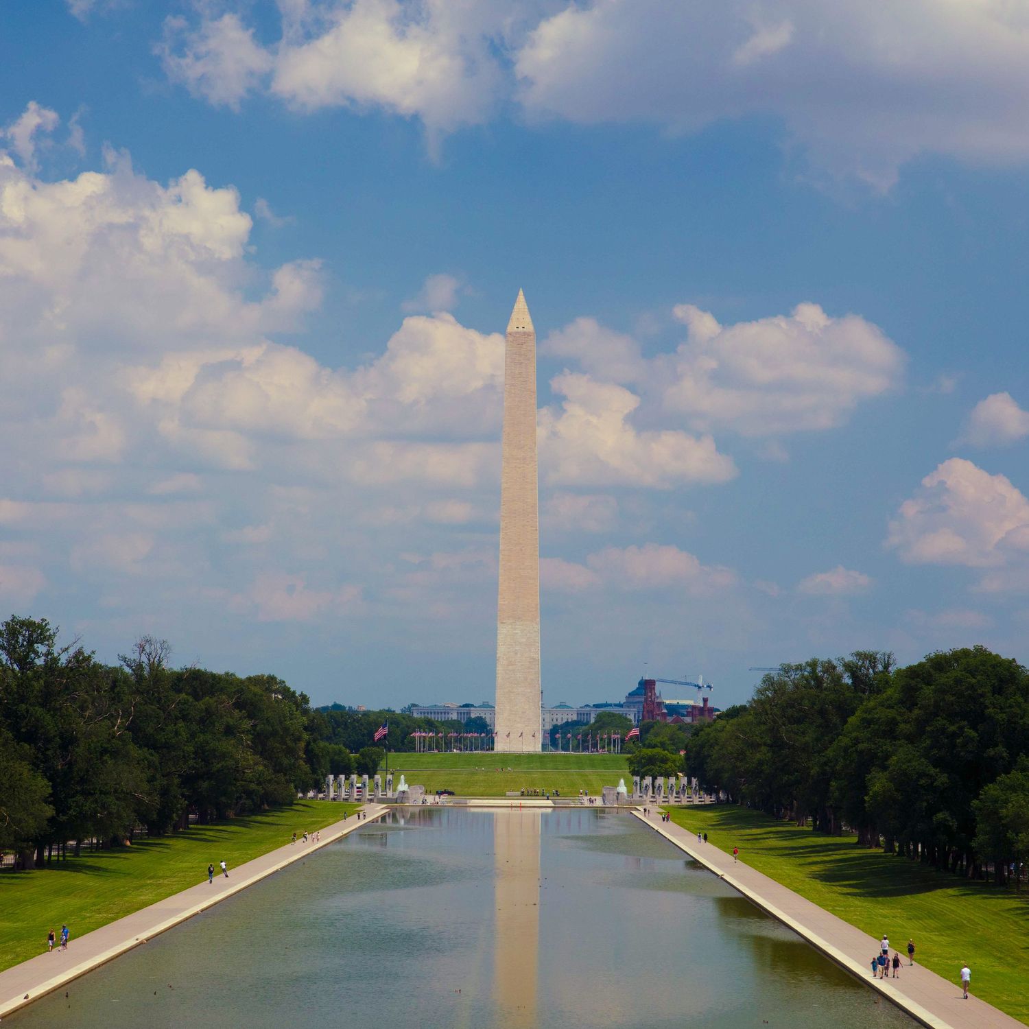 Washington Monument reflected in pool with blue sky and white clouds.