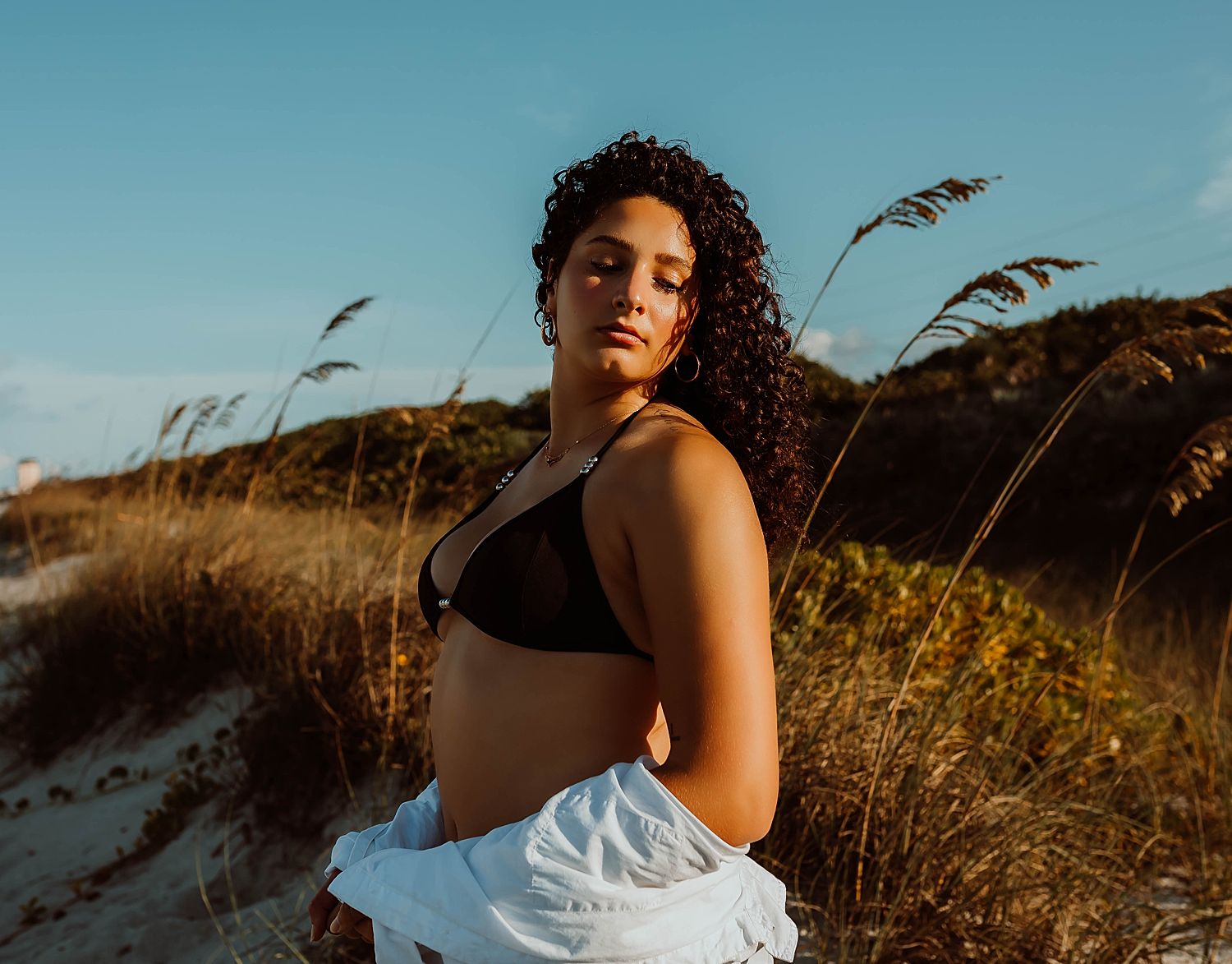 Woman with black curly hair in tall grass by Boudoir by KJ