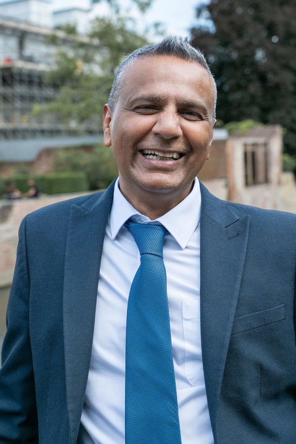Professional portrait series showing a person in a navy suit and bright blue tie smiling warmly against a blurred outdoor background.