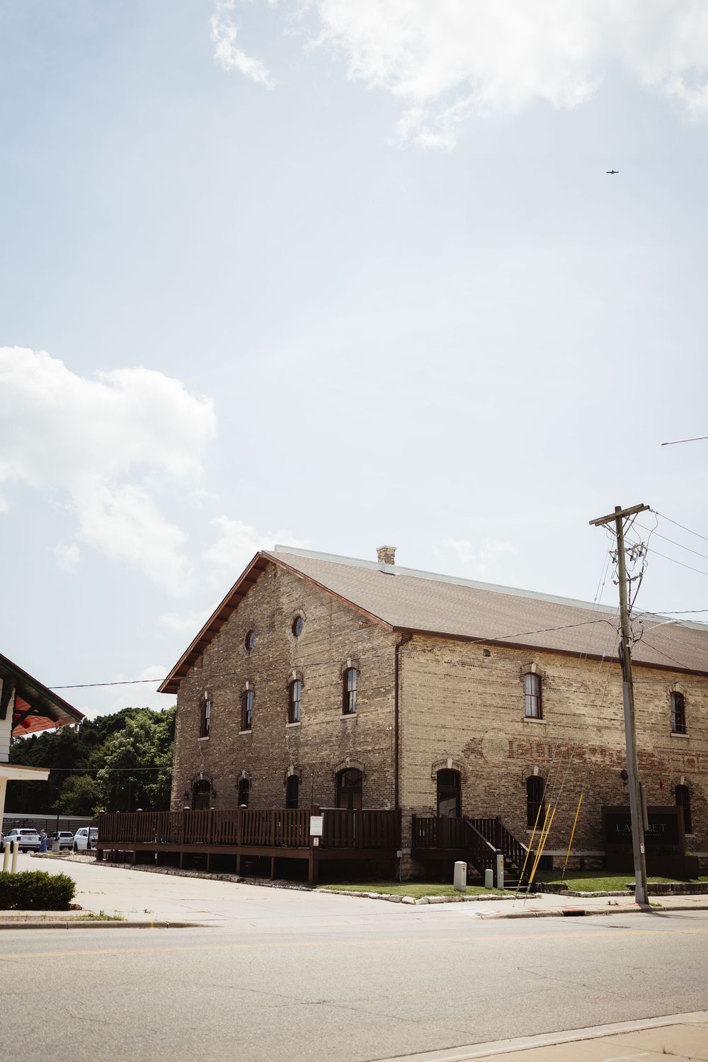 Historic stone warehouse buildings with arched windows and brick facades line a street corner under a cloudy sky.