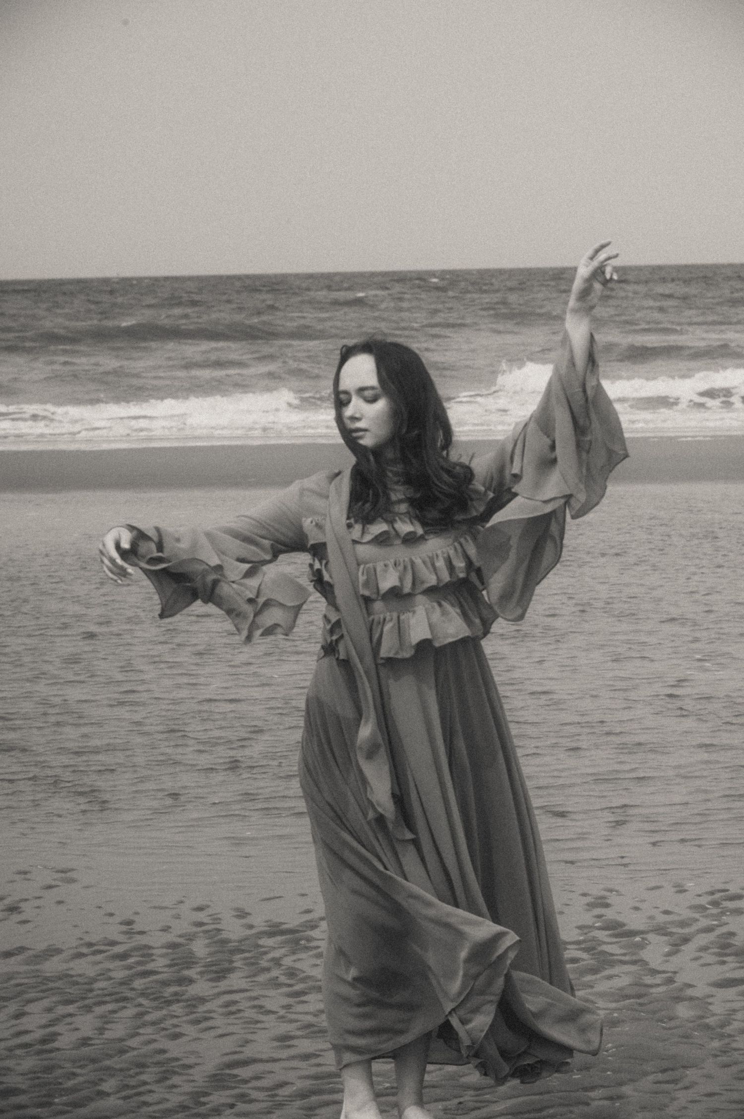 Woman in a flowing chiffon dress standing by the sea, hair blowing in the wind — soulful portrait session in the Netherlands.