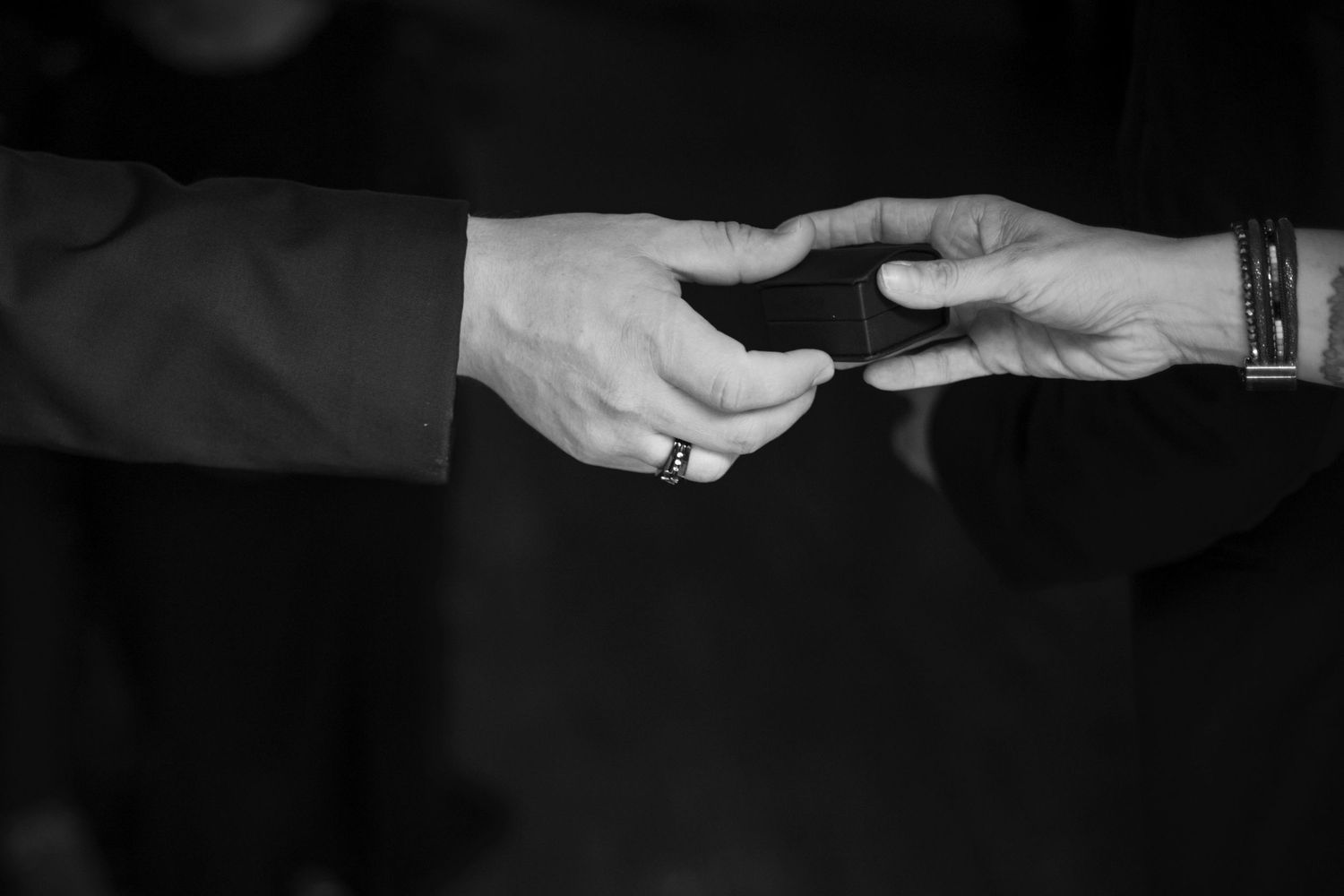 Two hands reaching towards each other exchanging an object in black and white dramatic lighting.