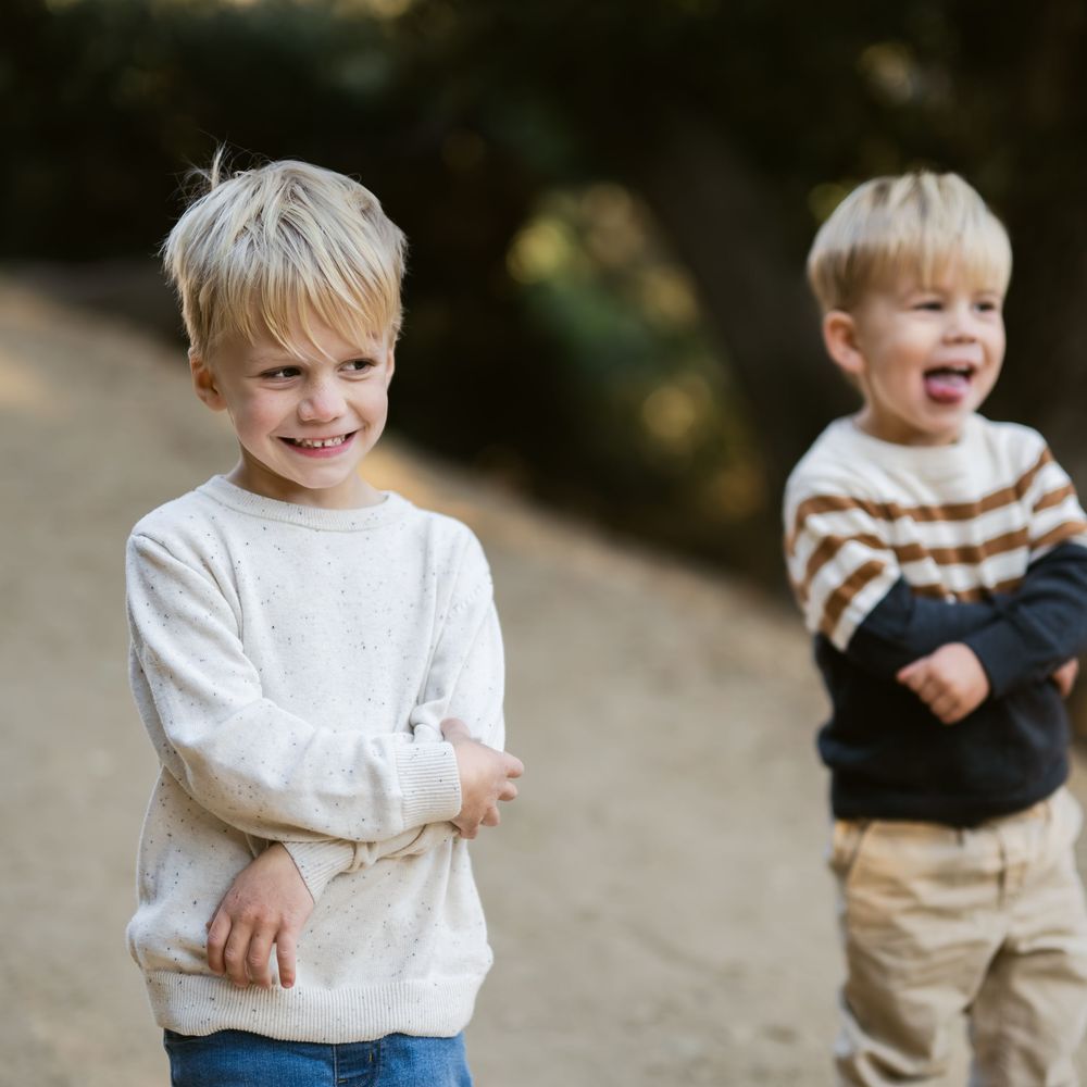 Two young children in sweaters playing and laughing together outdoors in natural light.