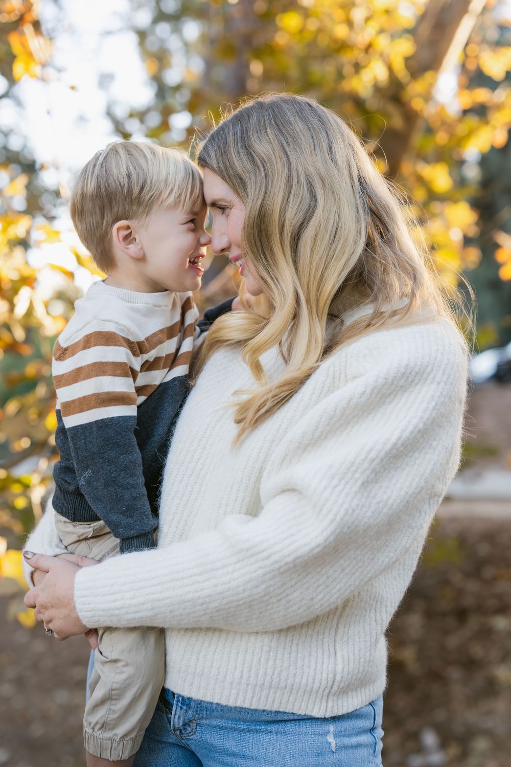 Tender moment shared between parent and child against autumn foliage background in matching white sweaters.