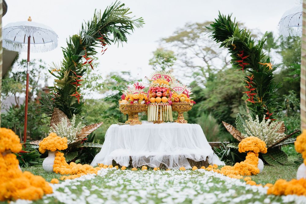 Festive table arrangement with orange flowers and tropical decor against natural backdrop.