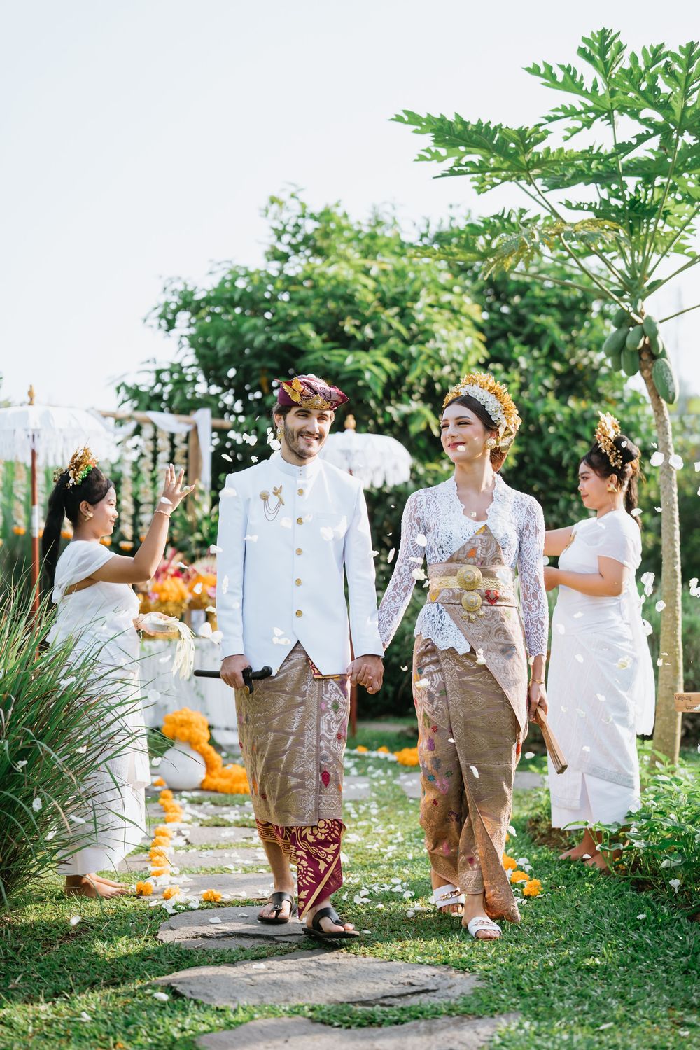 Traditional wedding ceremony in a lush garden setting with white and tan attire.