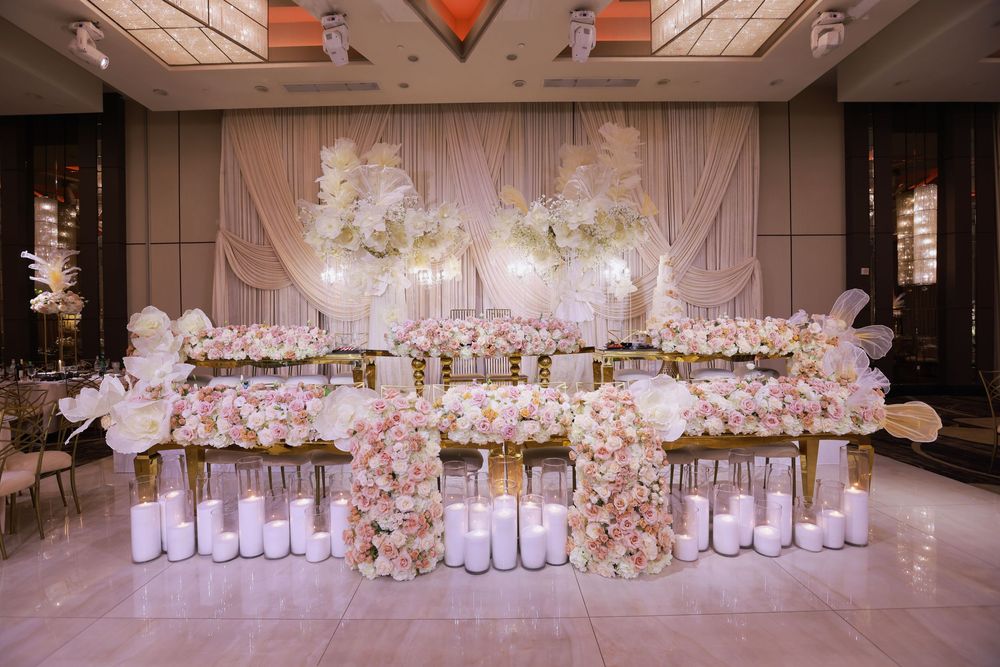 Luxurious wedding reception setup with elegant white floral arrangements and glowing candles along a grand banquet table.