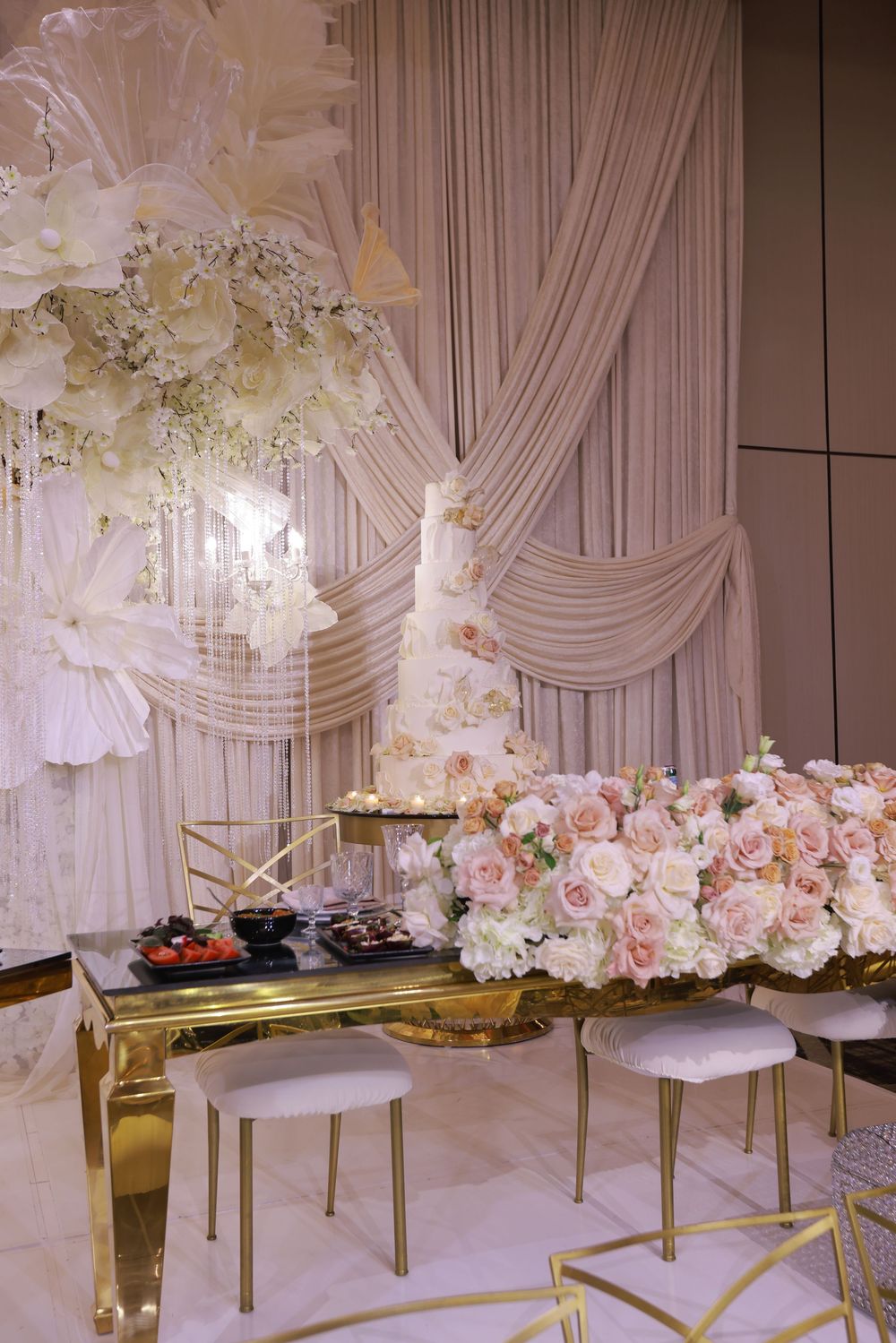 Elegant wedding reception setup with white draped backdrop and pink floral arrangements on gold tables.