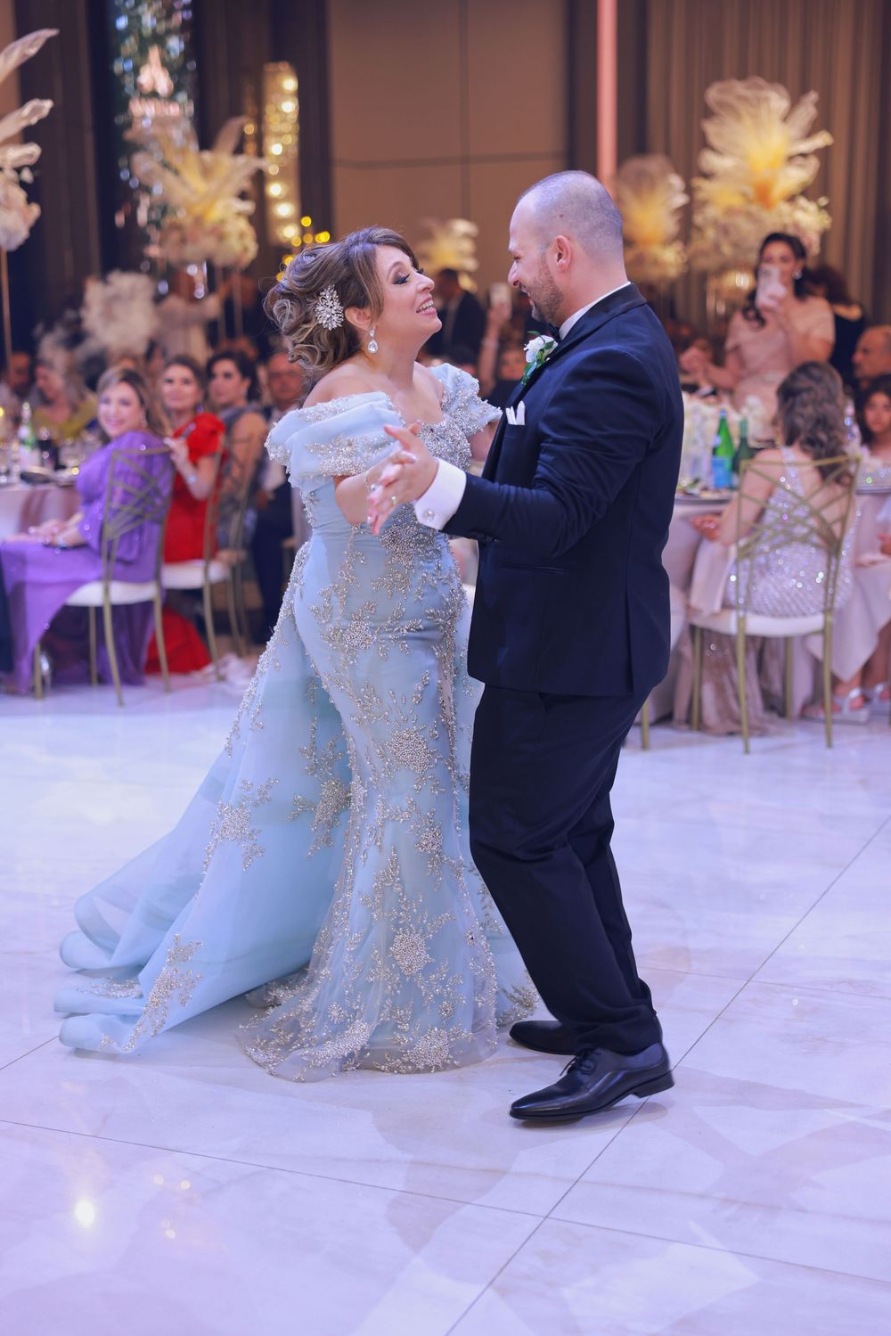 Newlyweds dancing together on a white marble dance floor at an elegant reception with guests watching.